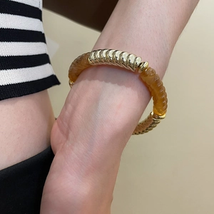 Close-up of golden threaded metal and amber resin segments bracelet worn on wrist