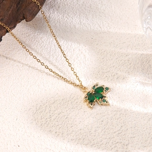 Detail showing the maple leaf pendant with green crystals and a gold chain necklace