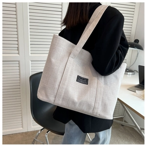 Detail of off-white large canvas tote bag showing textured fabric and a minimalist black label