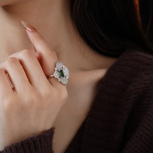 Detail of silver ring with green emerald-cut stone and white zircon flower setting
