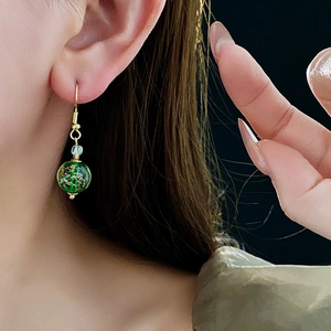 Detailed close-up of a model wearing a green glass bead earring with gold leaf inclusions