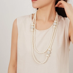 Detail view of a double-layer pearl necklace with rhinestone-encrusted spheres on a model