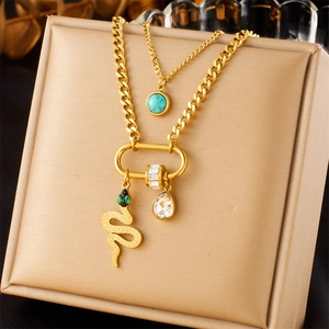 Detail of layered gold-plated necklace with snake pendant and emerald green stones