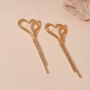 Detail of gold hollow heart earrings with elegant rhinestone tassels on beige background