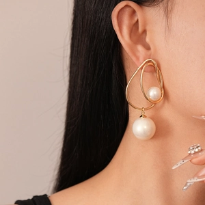 Close-up of golden geometric twisted earrings with white pearls on a model's ear