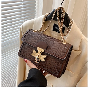Detail of dark brown snake pattern shoulder bag with golden bee buckle and metal chain