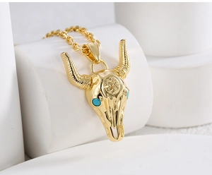 Macro shot of gold bull skull pendant with turquoise eyes and detailed engravings
