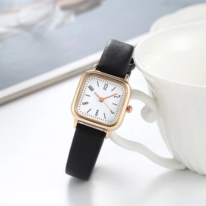 Elegant women's square watch with black leather strap and gold case on a white desk