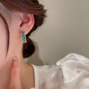 Macro shot of gold geometric earrings with blue and green pave zircons on female model