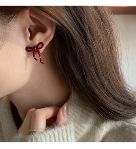 Close-up of a glossy red bow-knot stud earring worn by a model in soft lighting