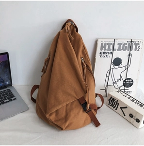 Detail of tan canvas sling bag with unique triangular cut on white desk with laptop