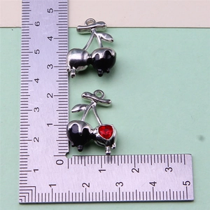 Detail view of two cherry-shaped DIY charms with red crystals and metallic finish
