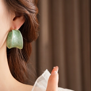 Detail of a vintage green marble pattern hoop earring worn by a model in soft lighting