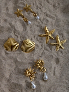 Detail of golden starfish and seashell earrings with pearls on a sandy beach