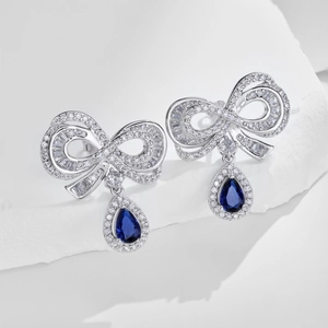 Macro detail of blue pear-shaped zircon stones and silver bow earrings on stone