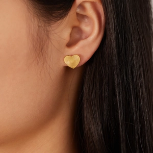 French vintage style heart stud earrings in gold with radial texture worn by a model