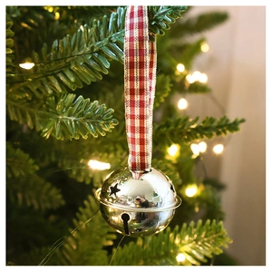 Detail of silver star cutout metal bell ornament hanging with red checkered ribbon on tree