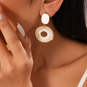 Close-up of model wearing gold woven circular geometric earrings with faux pearl detail