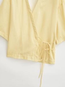 Detail of yellow and white striped wrap top showing textured fabric and side bow tie