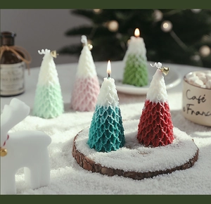 Close-up of a mini Christmas tree candle with snow texture and a gold bell decoration