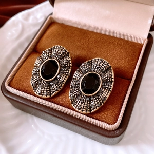Macro shot of vintage style gold oval earrings with black gemstones in a velvet box