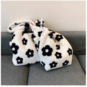Close-up of two black and white floral plush shoulder bags resting on a grey sofa