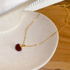Detail of a deep red bean-shaped pendant necklace with a gold chain on a ceramic tray