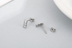 Close-up of silver rectangular textured stud earrings with matching backings on grey surface