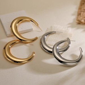 Detail view of gold and silver crescent hoop earrings on a textured surface