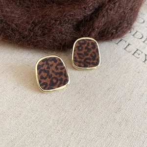 Vue macro des boucles d'oreilles peluche léopard avec bordure dorée sur fond de tissu