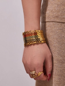 Stacked golden geometric checkerboard enamel bangles and sparkling zircon rings on wrist