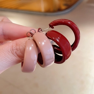 Close-up of thick C-shaped enamel hoops in burgundy and nude pink with glossy finish
