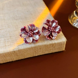 Détail de boucles d'oreilles fleur en résine violet foncé sur une boîte en lin beige