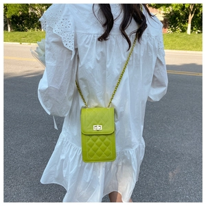 Detail of green quilted mini crossbody bag with golden chain strap on a white dress