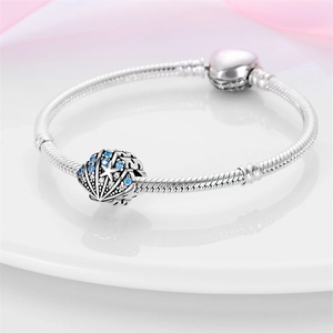 Silver shell charm bracelet with blue stones and starfish on a white display plate