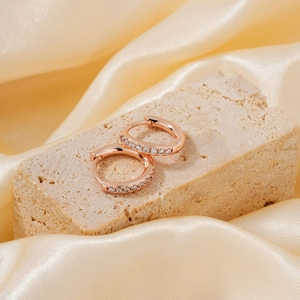 Rose gold hoop earrings with white zircon on beige stone with champagne satin background
