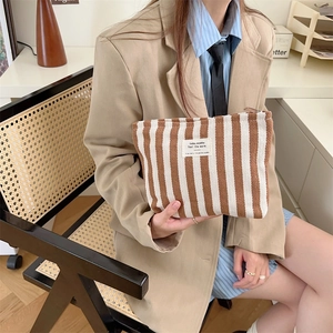 Detail of striped canvas toiletry bag held by a model in a minimalist blazer