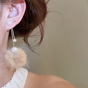 Detailed view of long earrings with white pearls, zircon accents, and beige fur balls