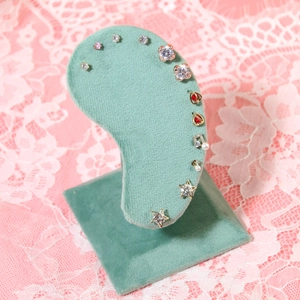 Green velvet ear-shaped display stand showcasing assorted gold-toned stud earrings