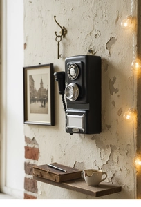 Detail of vintage wall-mounted black phone model with retro silver rotary dial on rustic wall