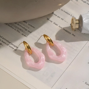 Detail view of pink marble resin earrings on vintage book pages with gold metal accents