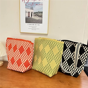 Three colorful checkered knit tote bags in orange, green, and black on a wooden table