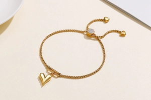 Detail of adjustable gold heart bracelet with slider clasp on a minimalist beige background