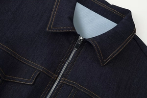 Détail de la veste en jean bleu foncé avec coutures contrastées et fermeture éclair en métal