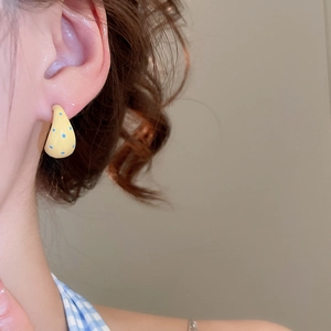 Close-up of yellow C-shaped earrings with blue dots worn on a model's ear lobe