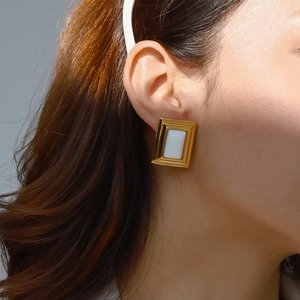 Detailed view of rectangular gold and white earrings worn on a model's earlobe