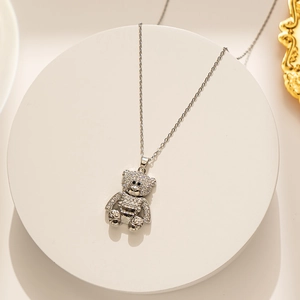 Detailed view of a silver teddy bear pendant with sparkling crystals on a white display stand