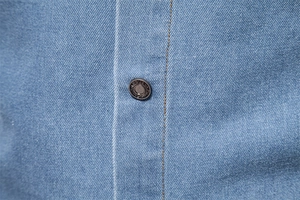 Macro detail of blue cotton denim shirt fabric with a fashion button and orange stitching