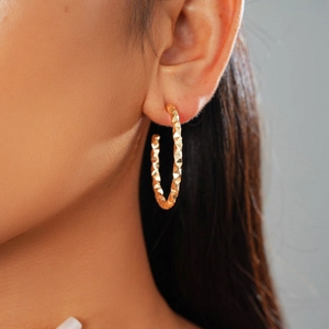 Close-up of golden C-shaped hoop earring with 3D geometric texture worn by a model
