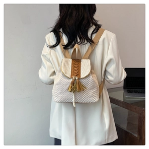 Detail of white straw backpack featuring brown leather accents and stylish tassels on back